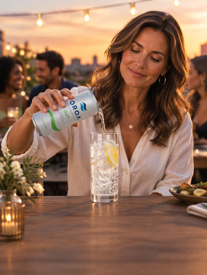 A woman pouring an OROA GUT can into a glass of ice at a rooftop dinner with friends